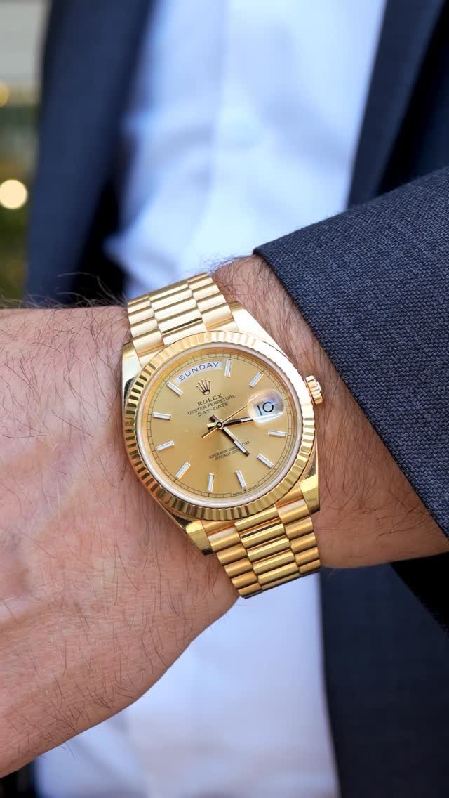 Gold Rolex watch on a wrist paired with a blue suit and white shirt