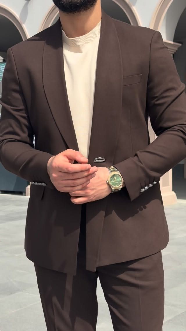 Man in a brown suit wearing a gold watch with a green face.