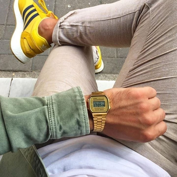 Gold-tone digital watch paired with a green jacket, beige pants, and yellow sneakers.