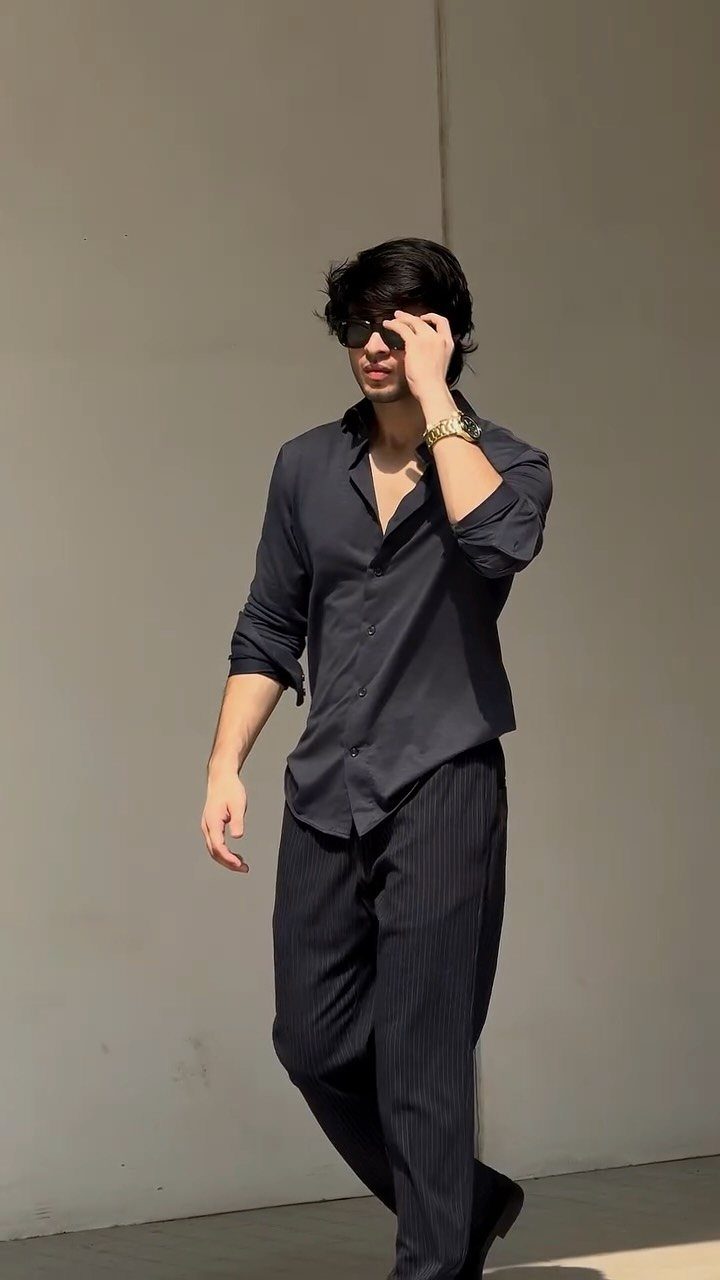 Man in navy shirt and pinstripe trousers wearing a gold watch and sunglasses.
