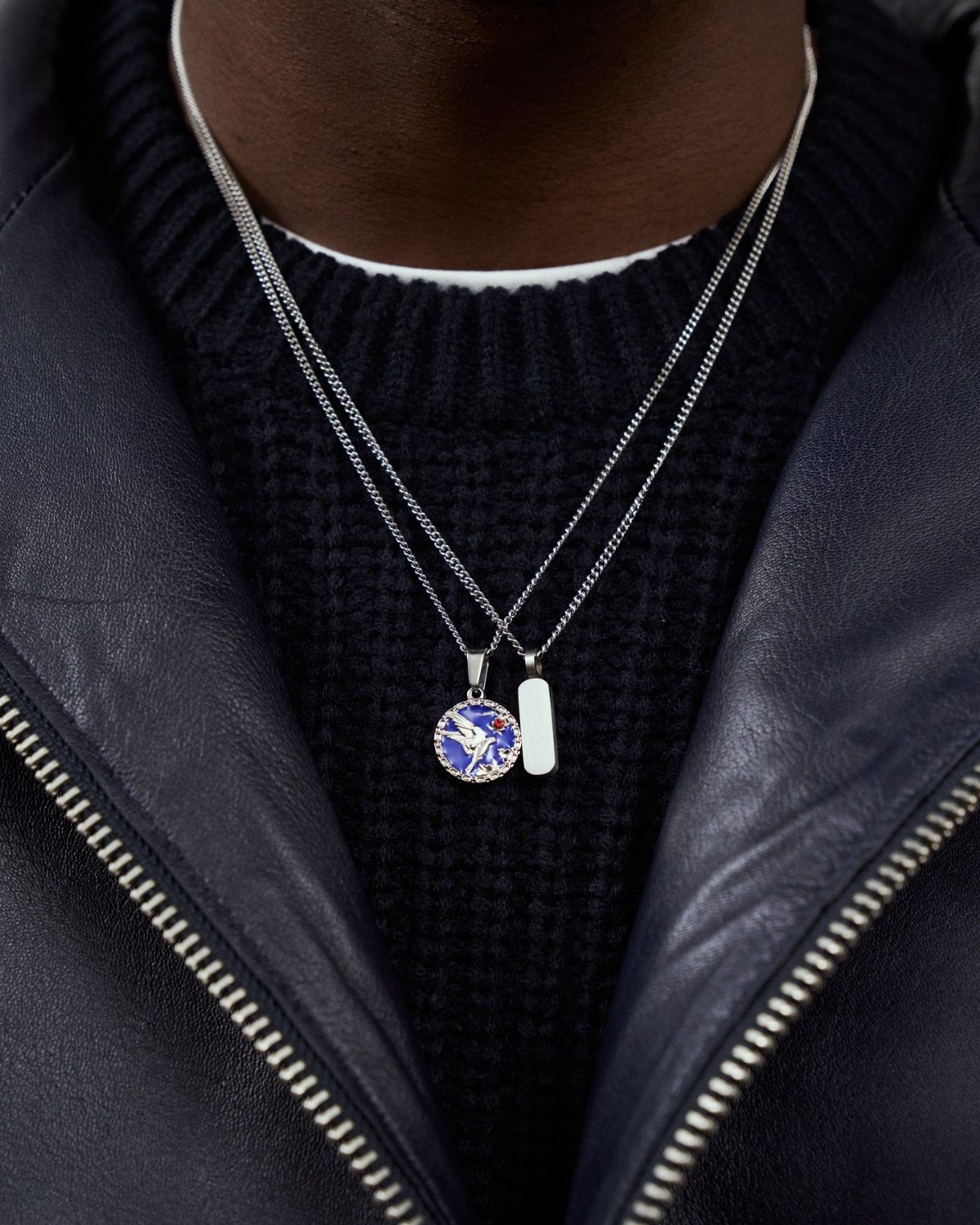 Man wearing layered silver chain necklaces with pendants over a black sweater and jacket
