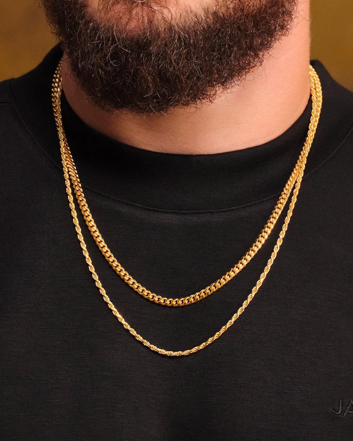 Man with a beard wearing two layered gold chain necklaces over a black turtleneck.