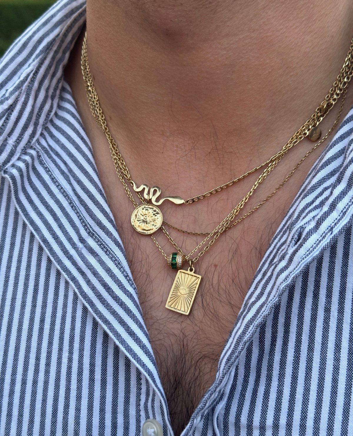Layered gold necklaces with pendants worn by a man in a striped shirt.