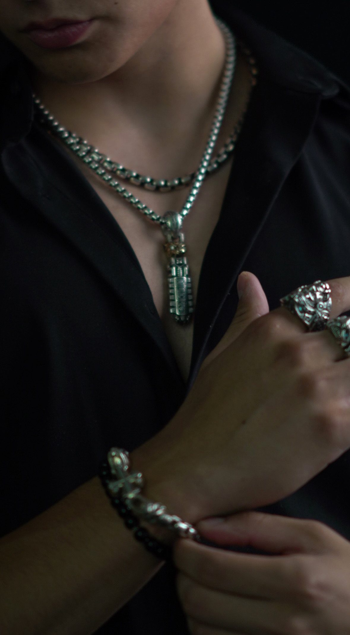 Man wearing layered silver necklaces and a pendant with a black V-neck shirt
