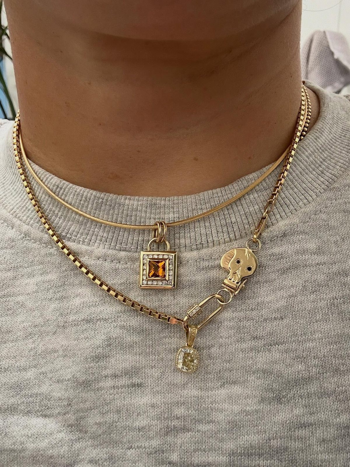 Three layered gold necklaces with pendants worn over a grey textured shirt.