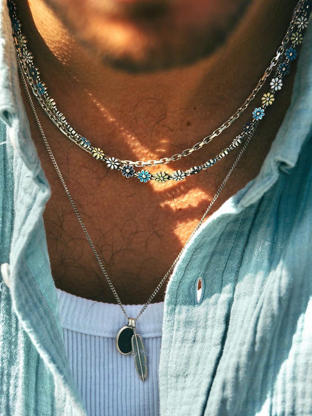 Three layered silver necklaces with flower charms and a feather pendant on a man