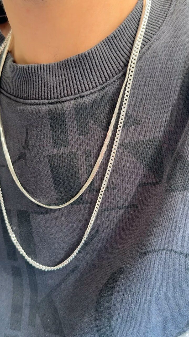 Two silver chain necklaces of different lengths layered over a grey sweatshirt.