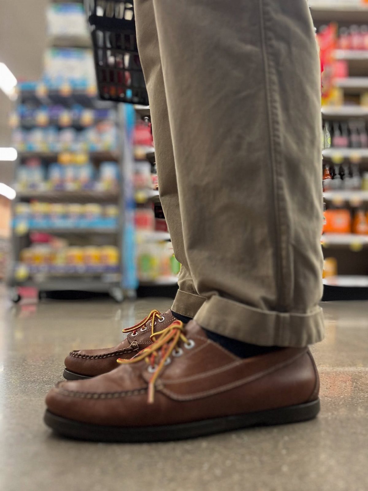 Brown leather boat shoes paired with rolled-up khaki chinos in a store setting.