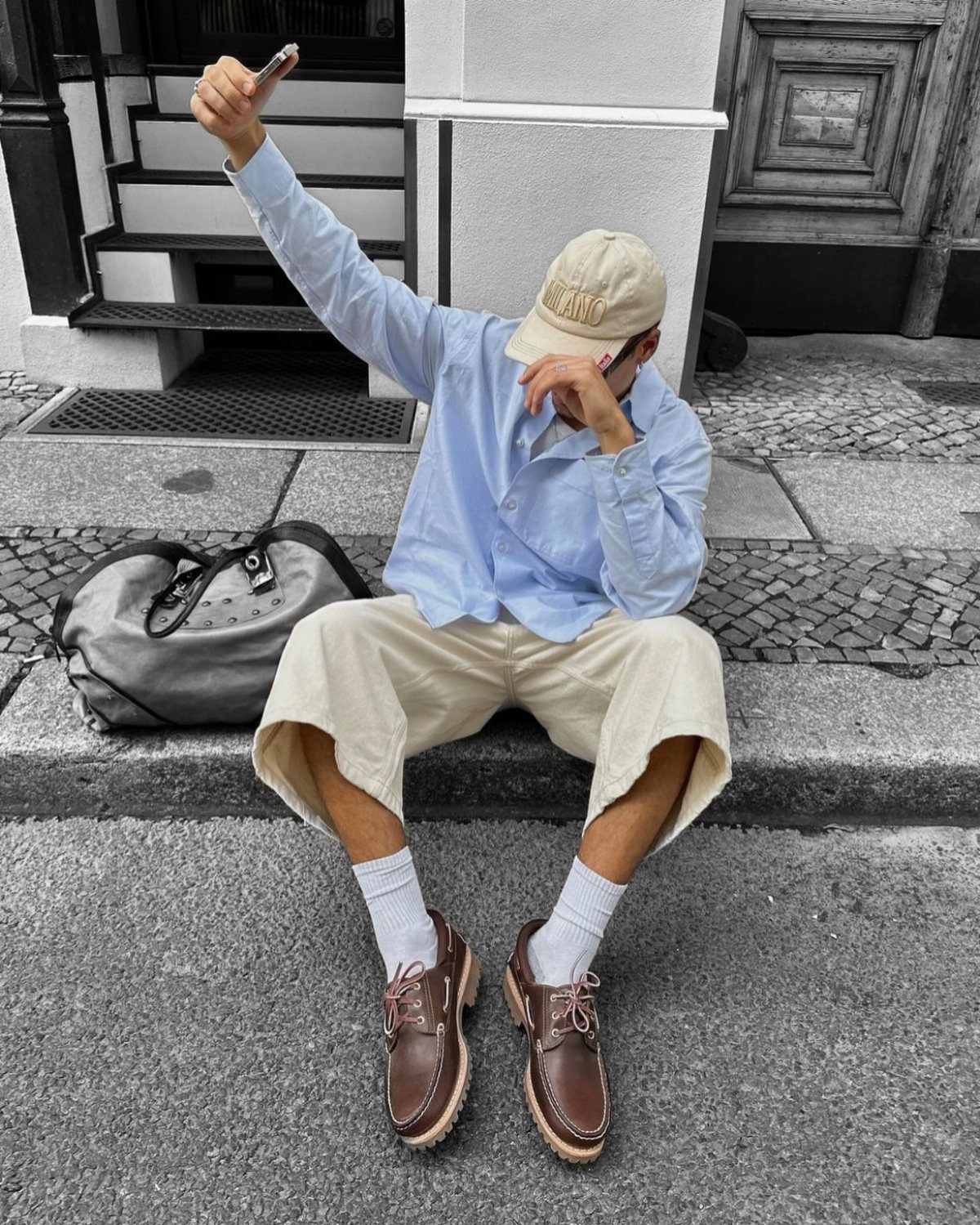 Man wearing brown boat shoes, beige shorts, and a light blue button-down shirt.