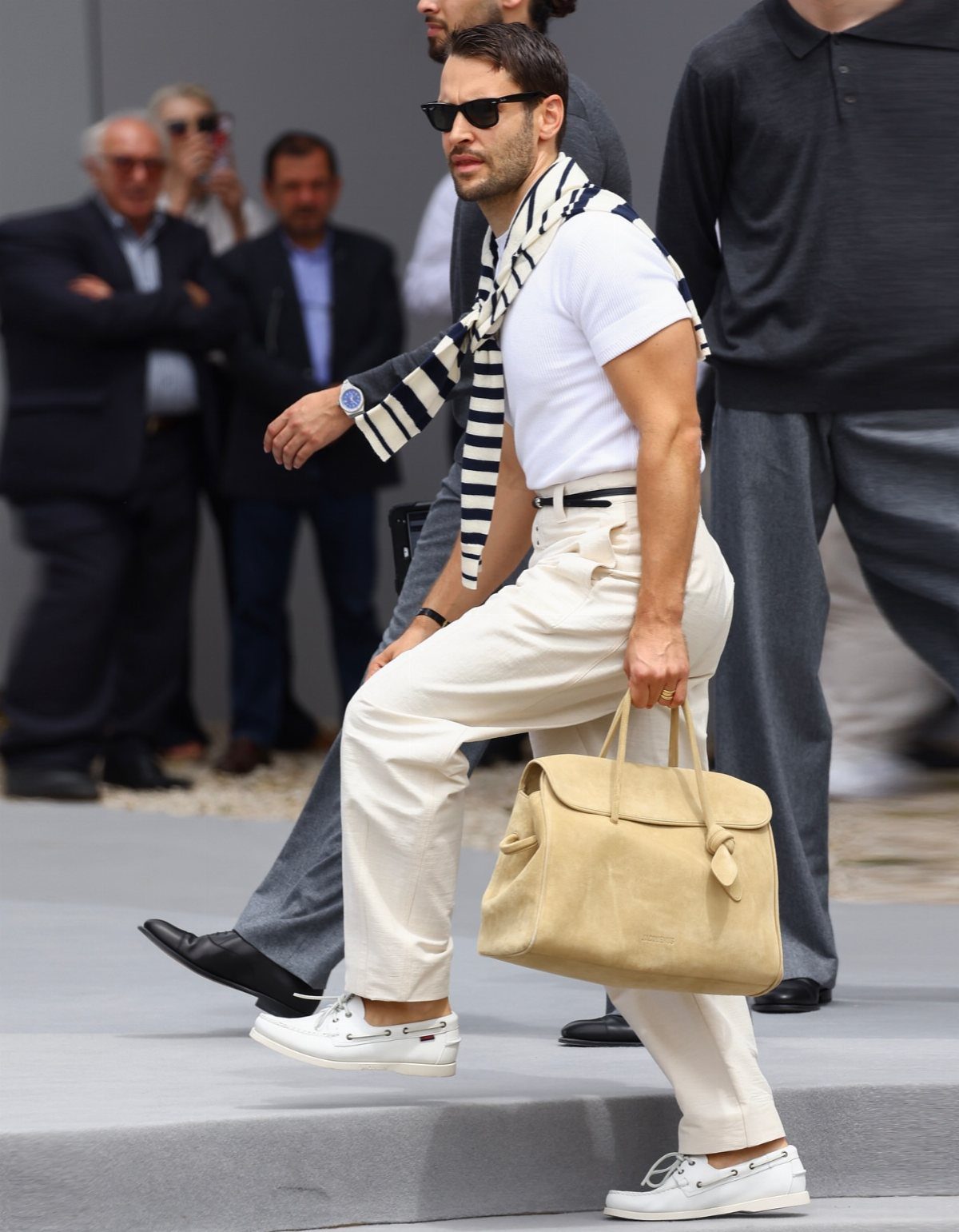 Man in white boat shoes and off-white trousers walking on a fashion runway.