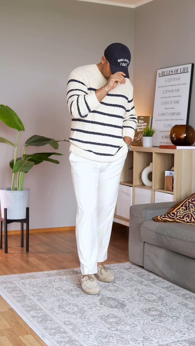 Man wearing a striped sweater, white trousers, and beige shoes in a living room.