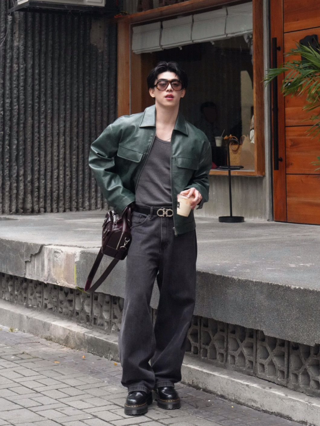 Man in green leather jacket and wide grey trousers wearing black chunky boots.
