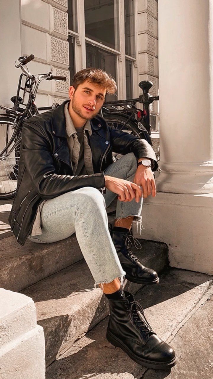 Man sitting on steps wearing a black leather jacket and black combat boots.