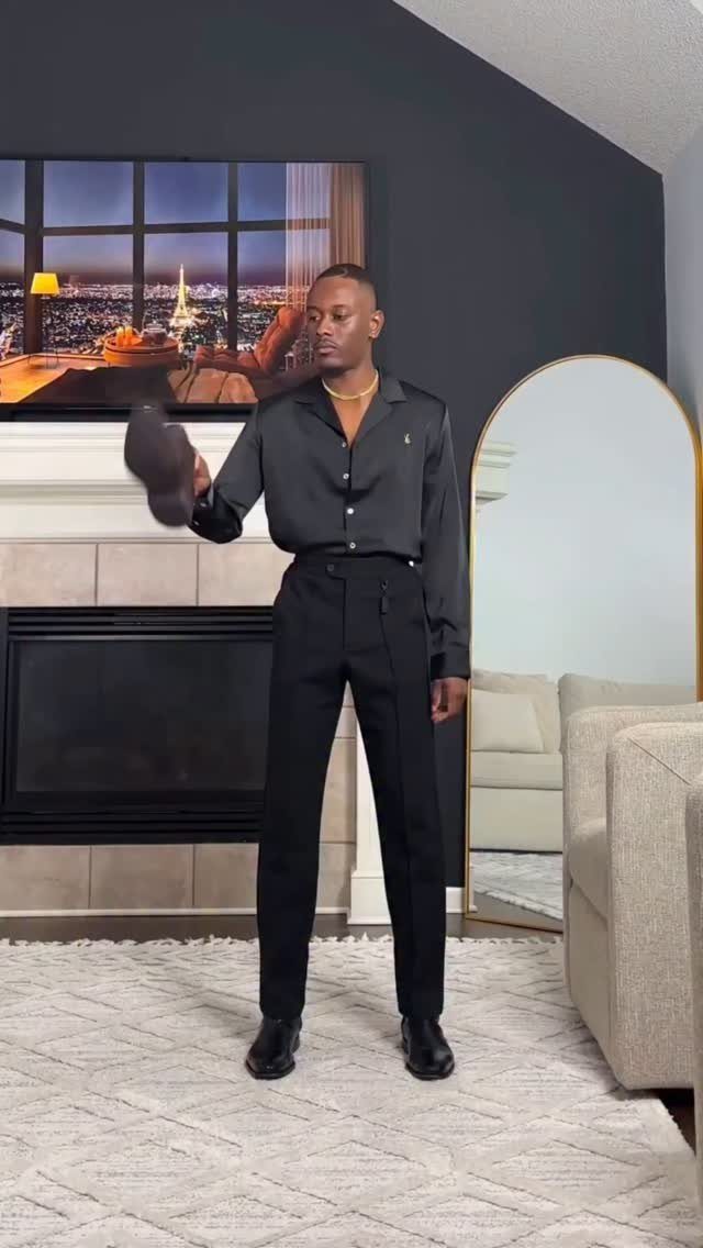 Man in all-black outfit with boots standing in a modern living room
