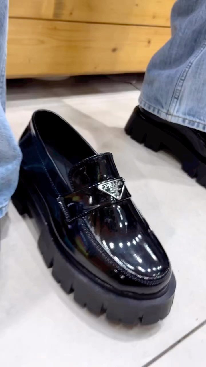 Black patent leather loafers with chunky soles paired with blue denim jeans.