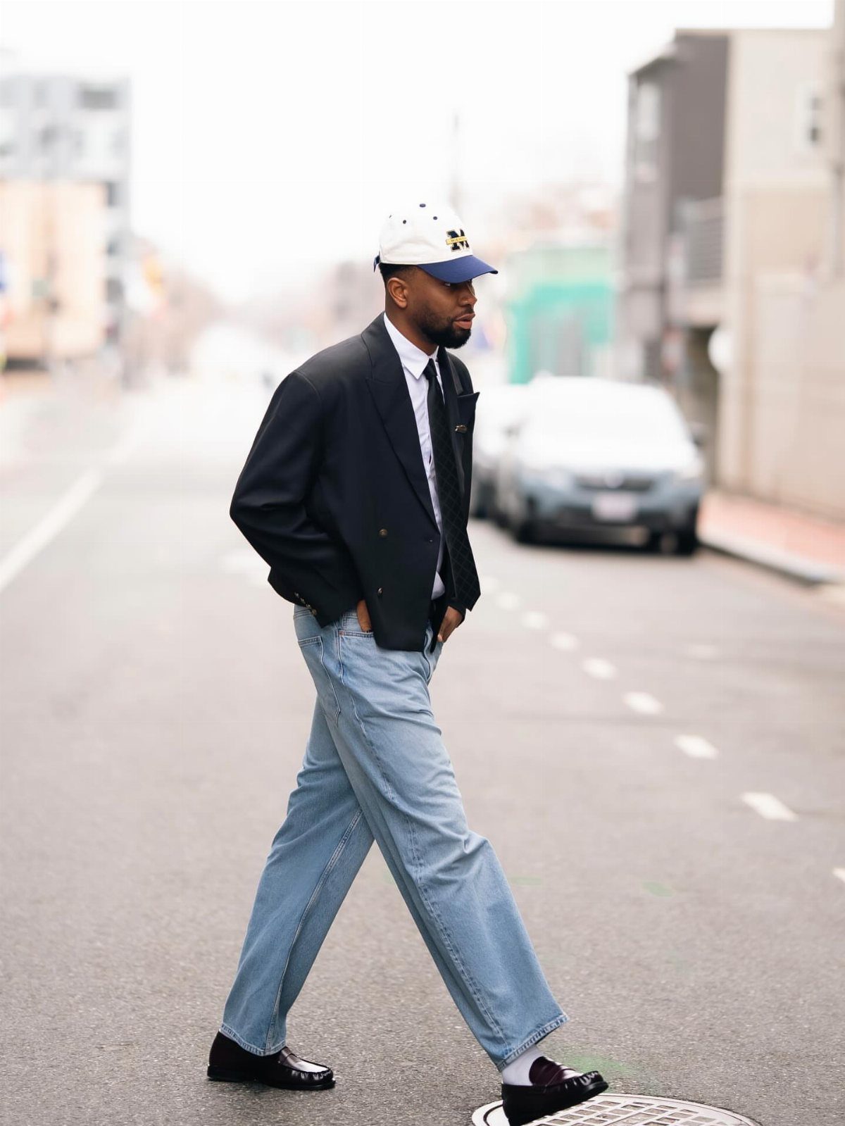 Man in black blazer and light-wash jeans walking in black loafers on street