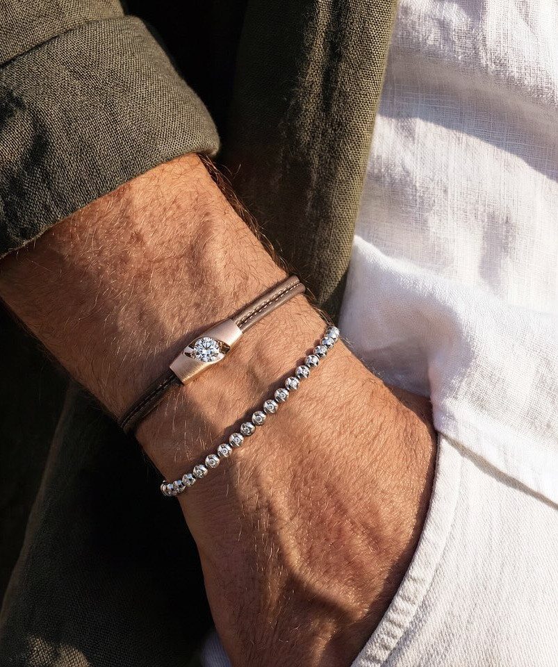 Two minimalist bracelets, one leather with a diamond and one silver beaded, on a wrist.