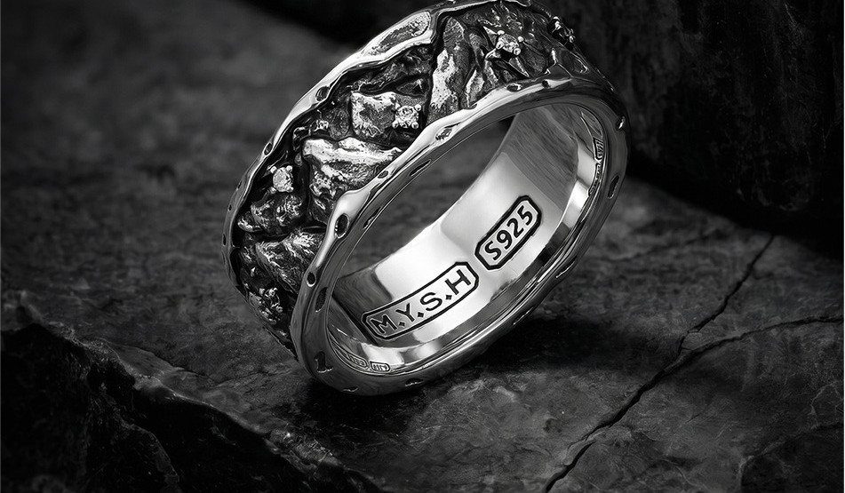 Silver ring with organic rock-like texture resting on a dark stone surface