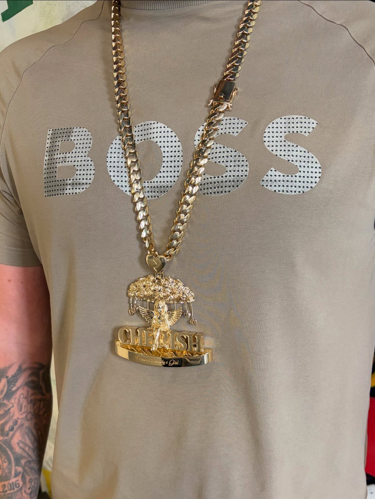 Gold curb chain necklace with a large custom gold pendant on a tan shirt