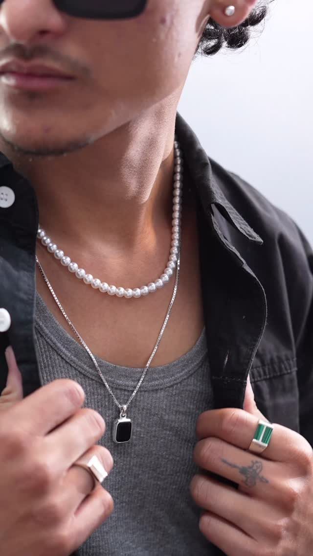Man wearing a white pearl necklace and silver jewelry with a black shirt.
