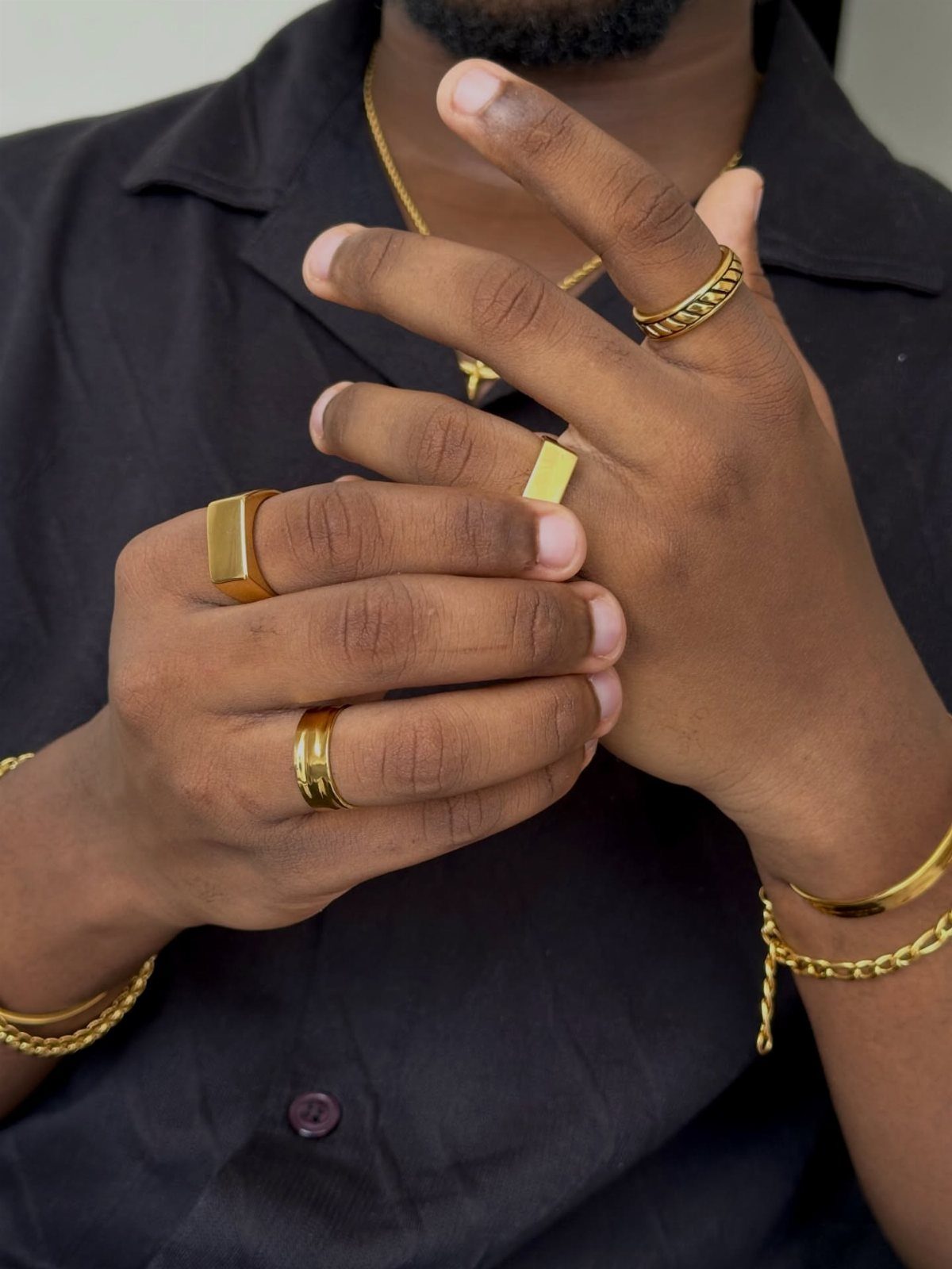Gold rings, bracelets, and a necklace worn by a person in a black shirt.