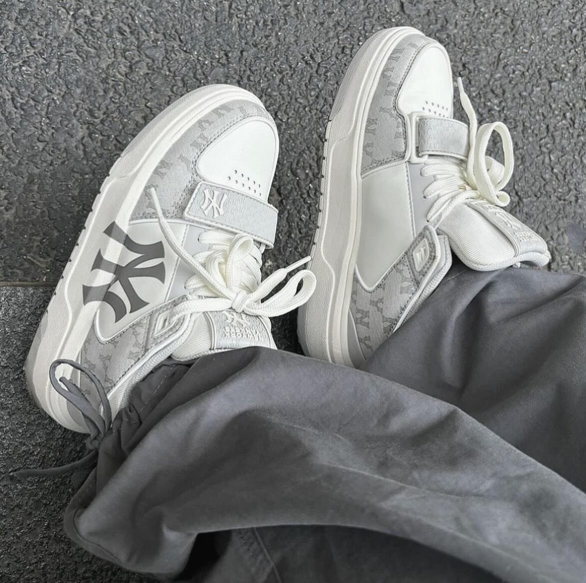 White and grey chunky sneakers with NY logos worn with grey trousers.