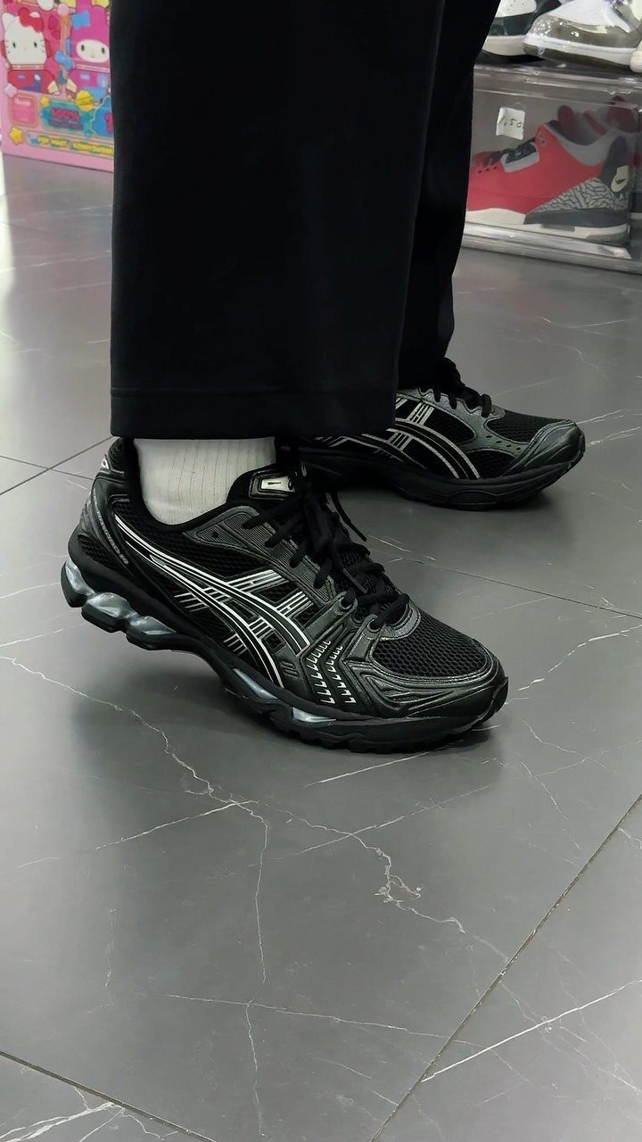 Black sportswear sneakers with silver accents worn with black trousers and white socks.