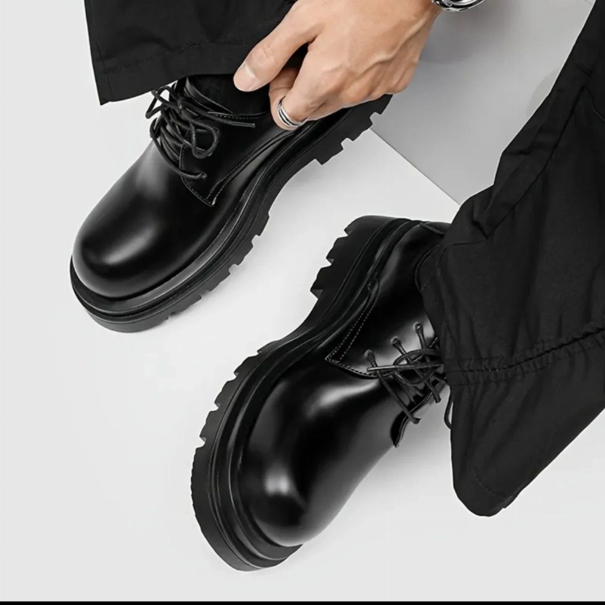 Chunky black leather lace-up shoes with thick soles worn with black trousers.