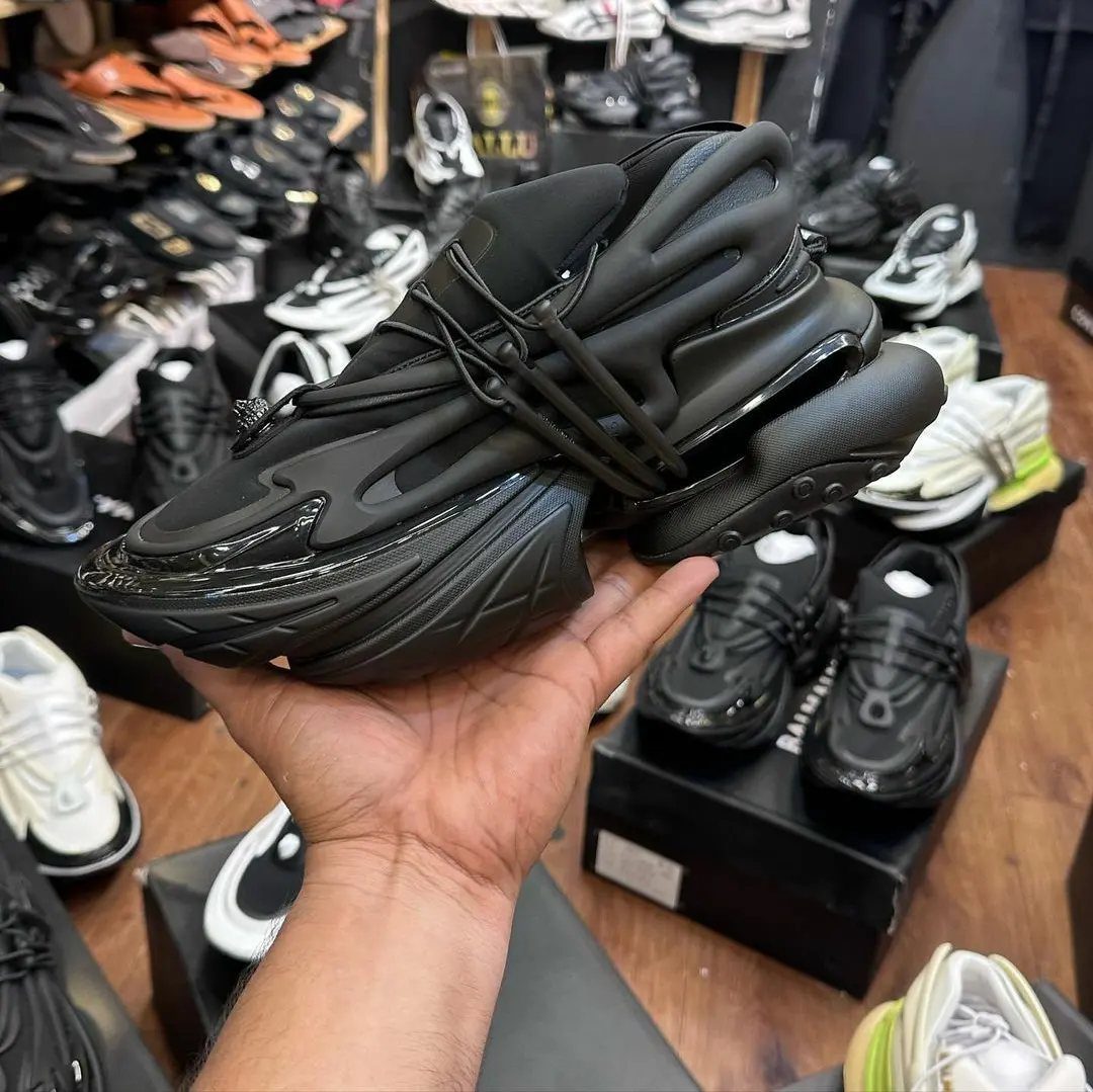 Black chunky futuristic sneaker held in a hand inside a shoe store