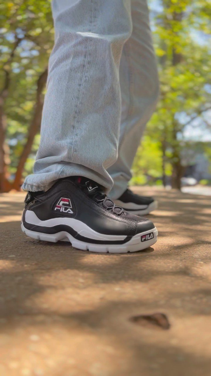Black FILA sneakers with white soles worn with light blue jeans outdoors.