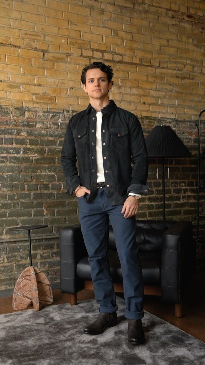 Man wearing a black shirt, blue trousers, and dark brown leather Chelsea boots.