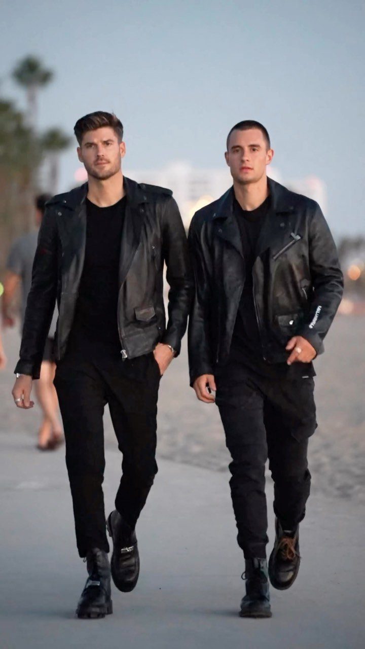 Two men in black leather jackets and boots walking on a paved path.