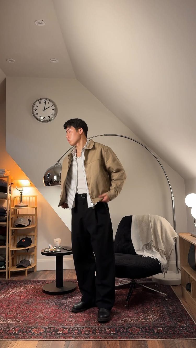 Man wearing a tan jacket, black trousers, and black leather boots in a room.