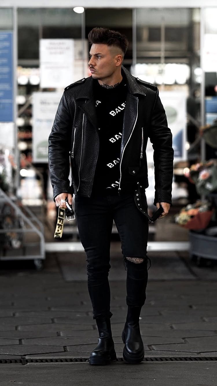 Man wearing a black leather jacket, black ripped jeans, and black leather boots.