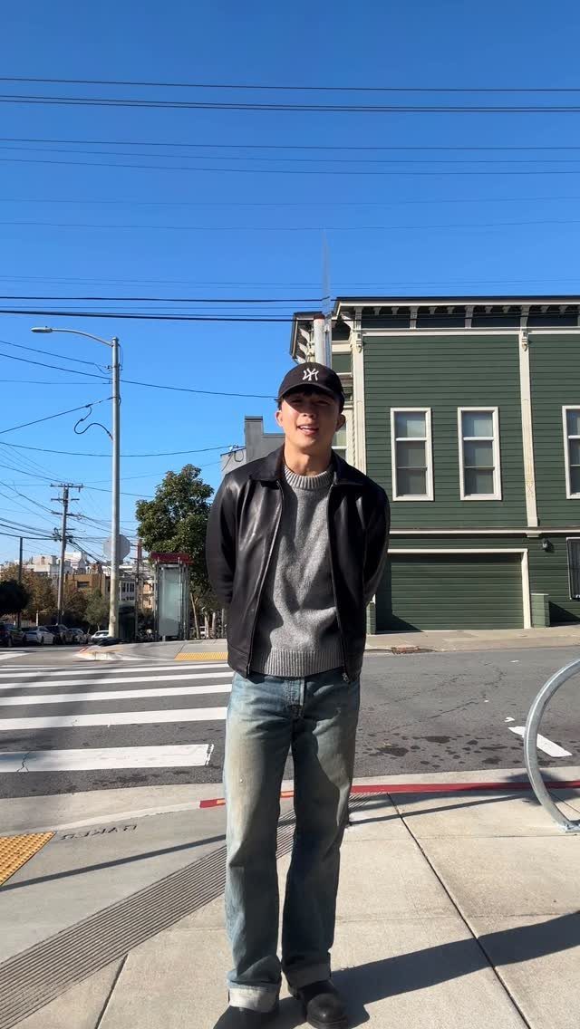 Man wearing a black leather jacket, blue jeans, and black boots on a sidewalk.