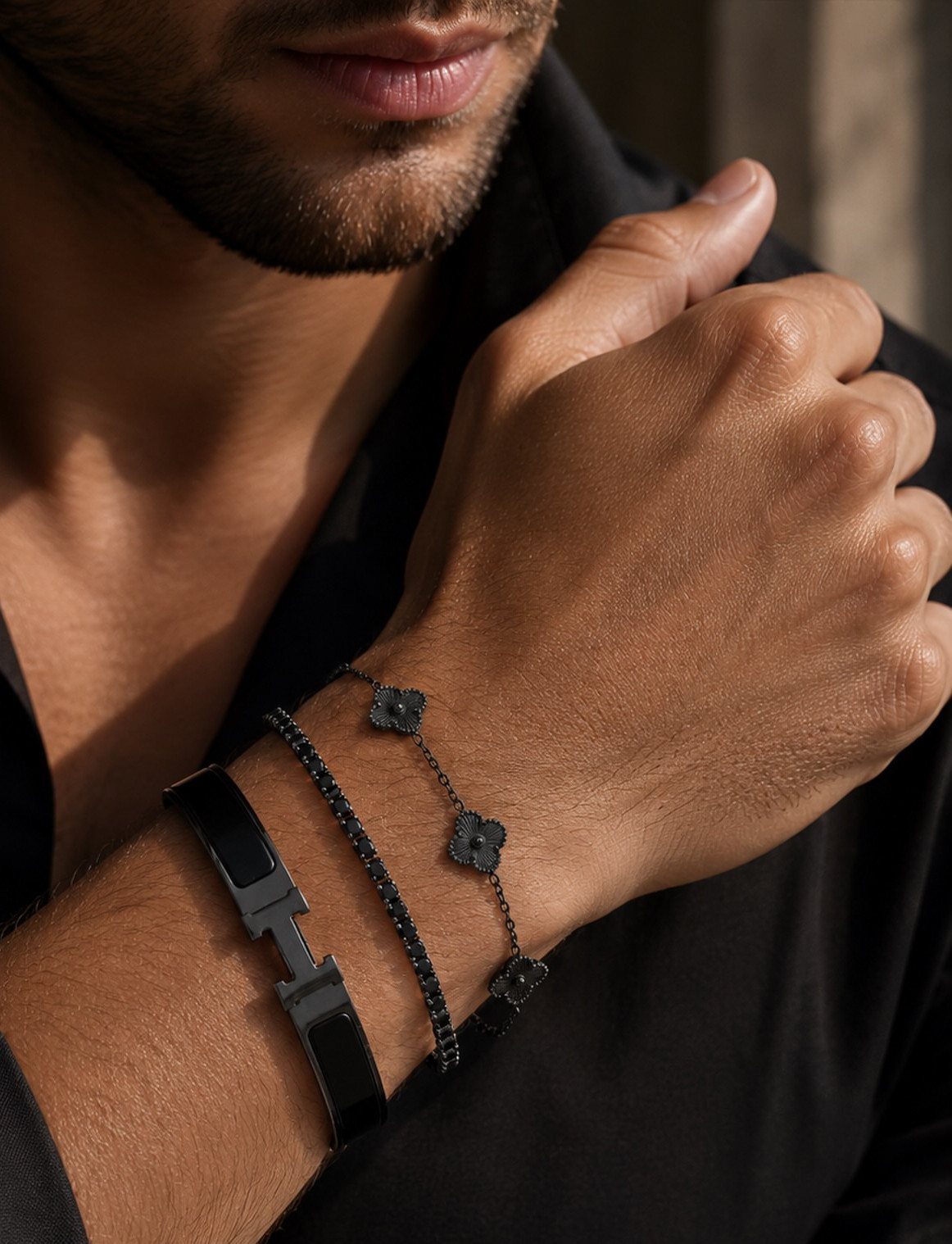 Man's wrist wearing a stack of three black bracelets and a black shirt.