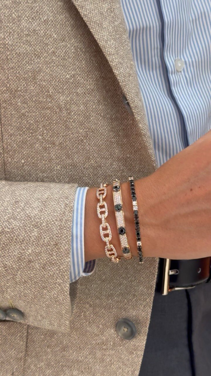 Man's wrist wearing a stack of gold and black bracelets with a blazer.