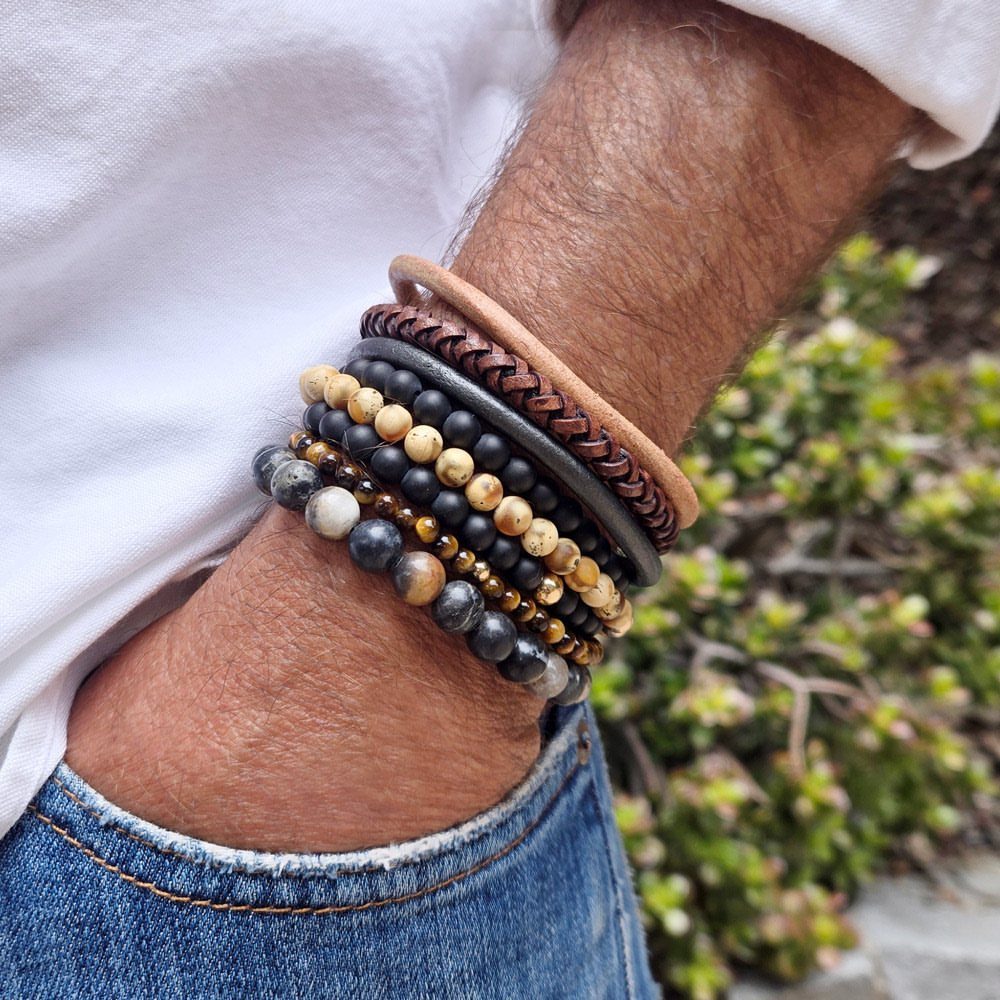 Man's wrist wearing a stack of leather, beaded, and braided bracelets with jeans.