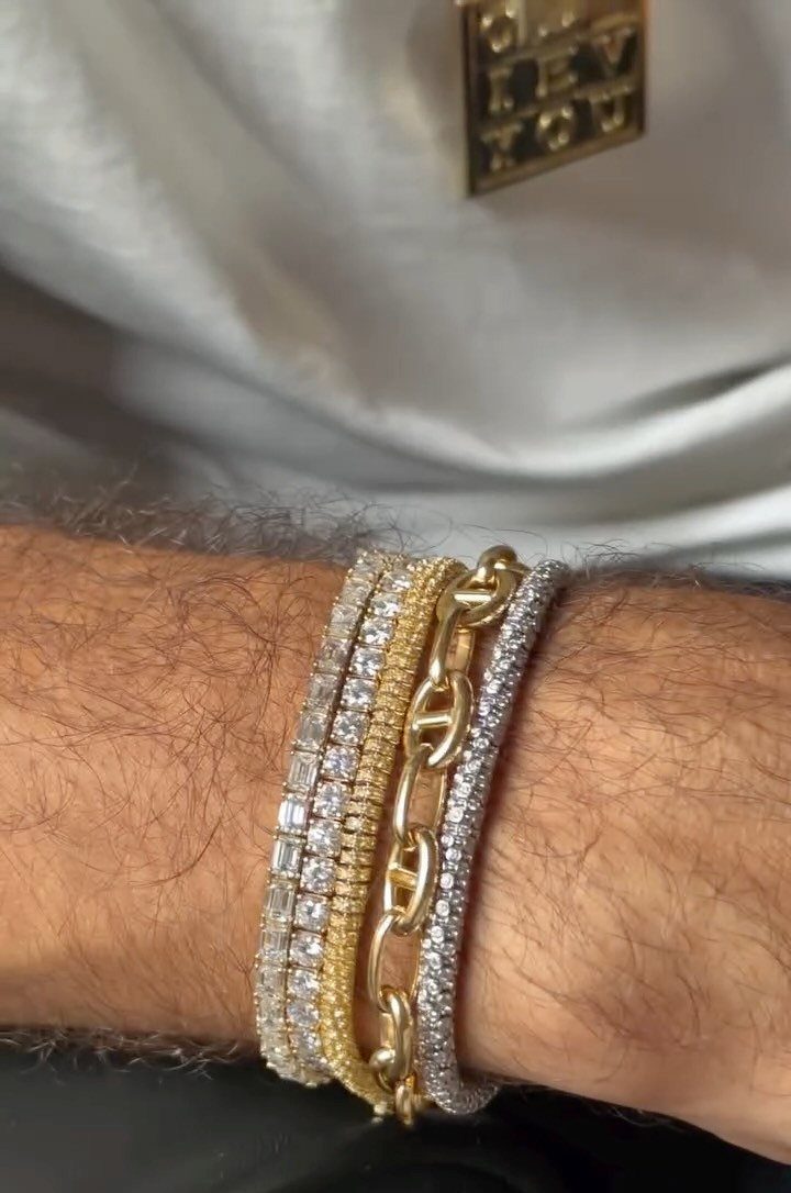 Man's wrist wearing a stack of gold and silver sparkling chain bracelets.