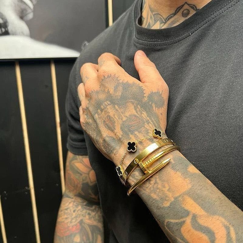 Tattooed wrist wearing a stack of gold chain and bangle bracelets.