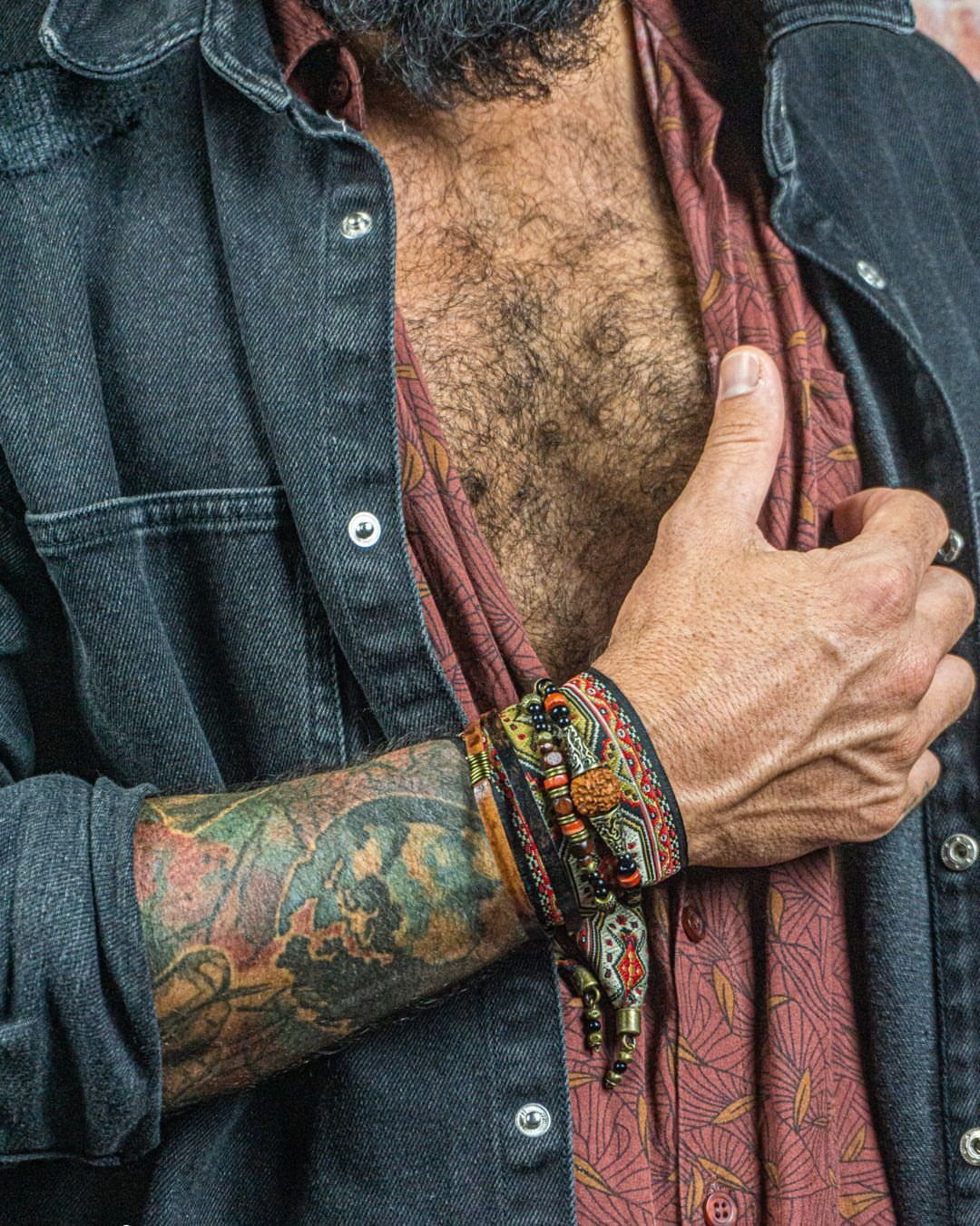Tattooed forearm wearing a stack of beaded and braided cord bracelets.