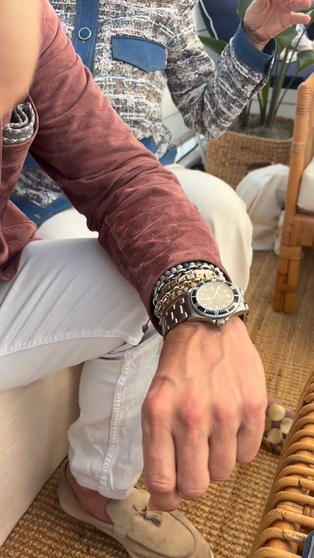 Man's wrist wearing a silver watch and a stack of mixed metal bracelets.