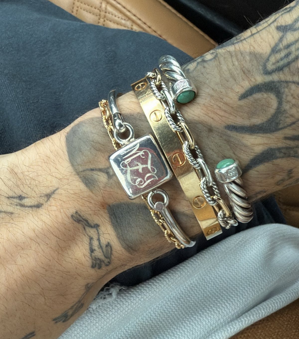 Tattooed wrist wearing a stack of gold and silver chain and bangle bracelets.