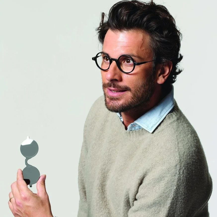 Man with a beard wearing black round glasses and a beige sweater.