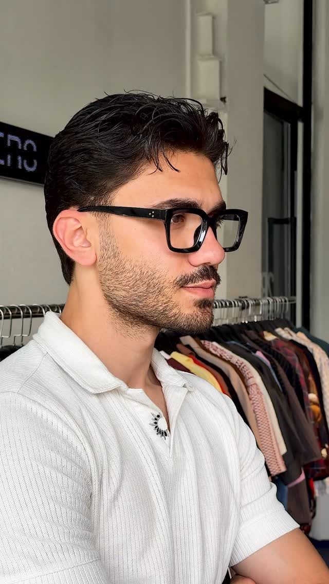 Man with dark hair and beard wearing thick black-rimmed glasses and white polo.