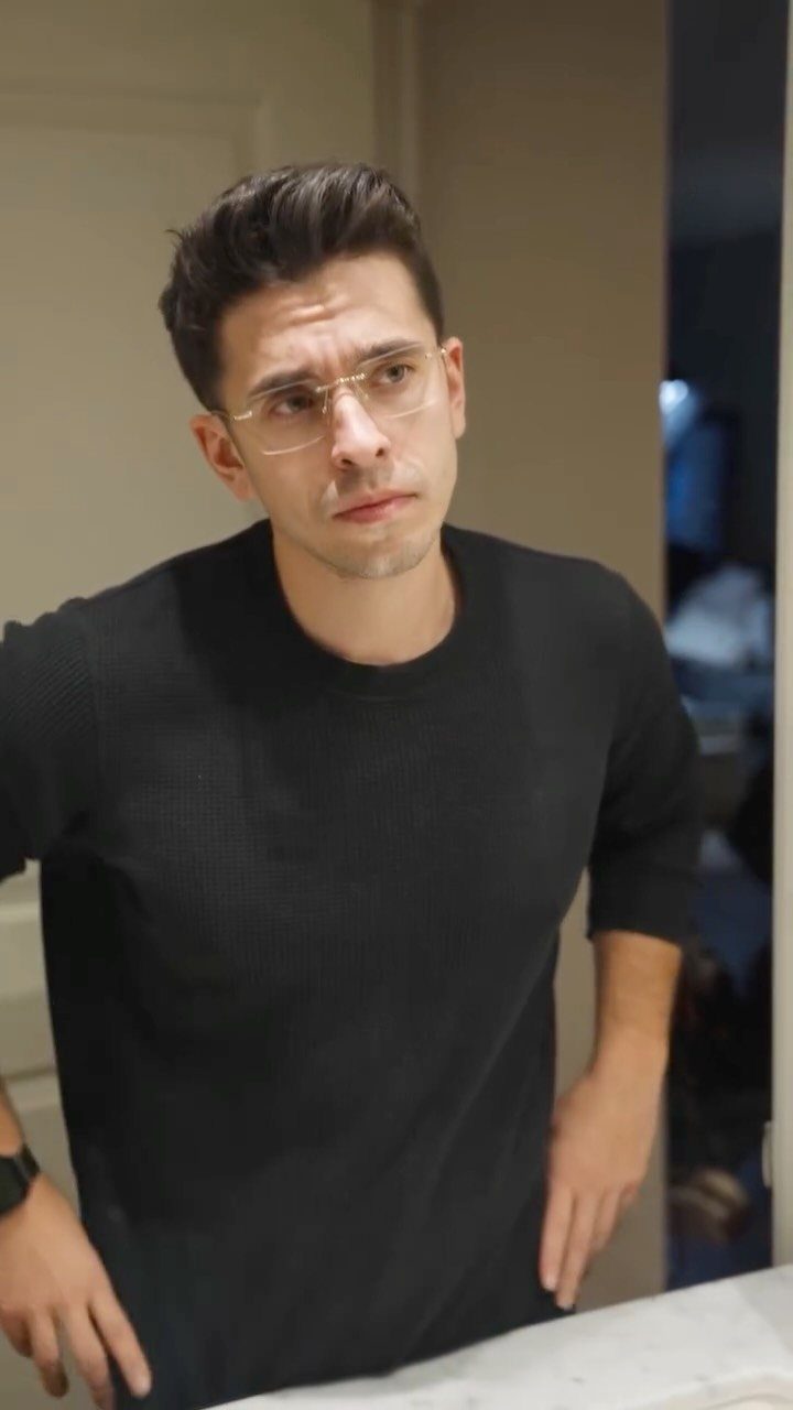 Man wearing thin gold-framed glasses and a black sweater looking to the side.