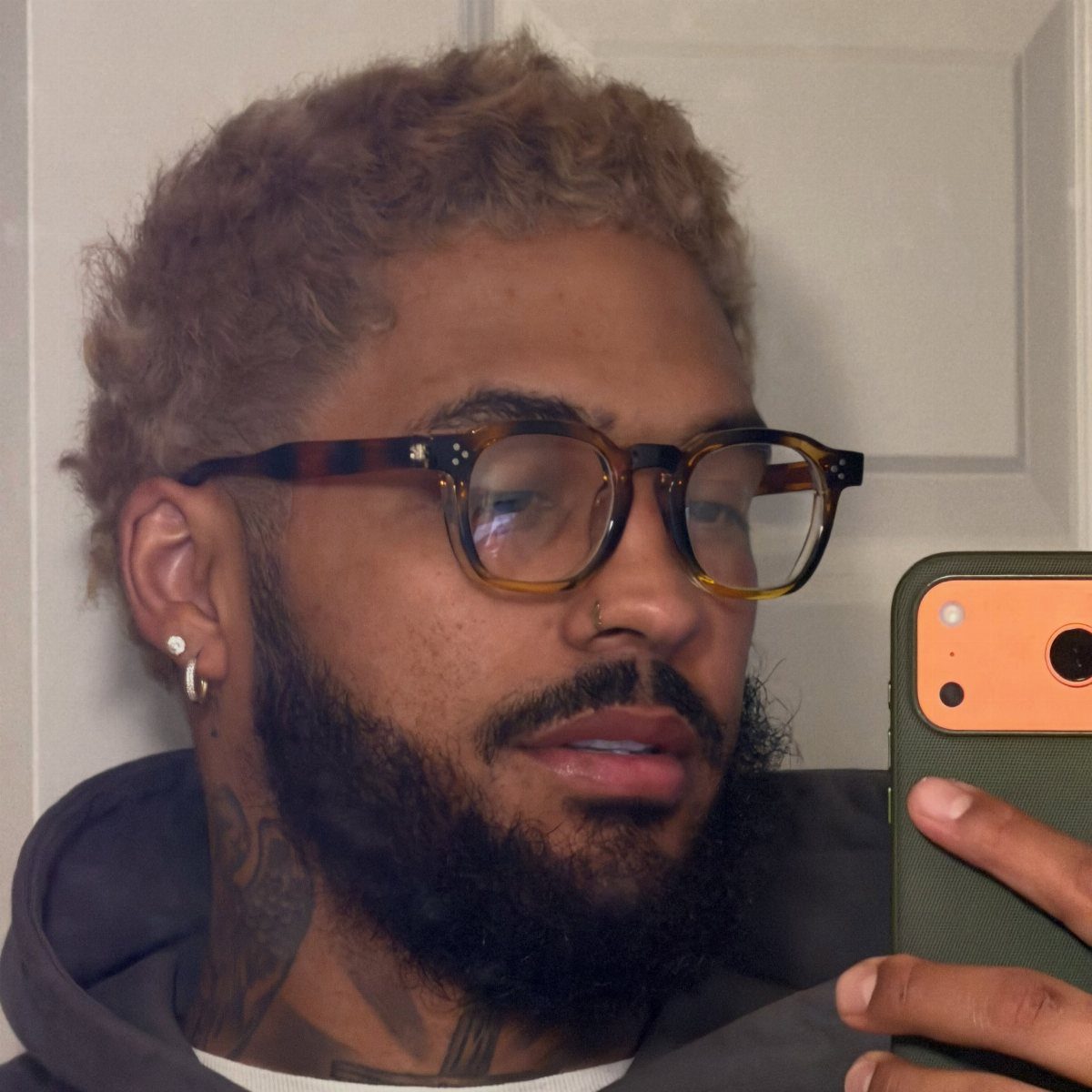 Man with curly hair and beard wearing tortoiseshell glasses taking a mirror selfie.