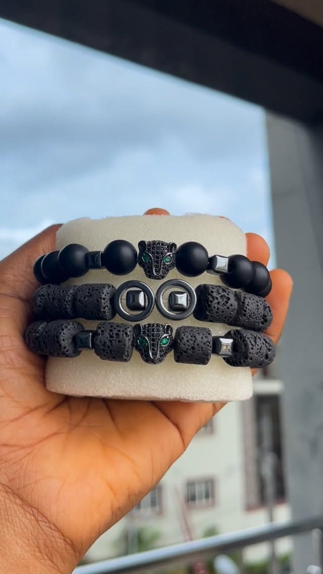 Three black beaded bracelets with panther charms displayed on a white foam stand.