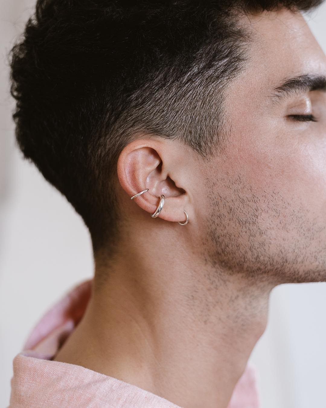 Man's ear with three silver hoop earrings in the lobe and cartilage.