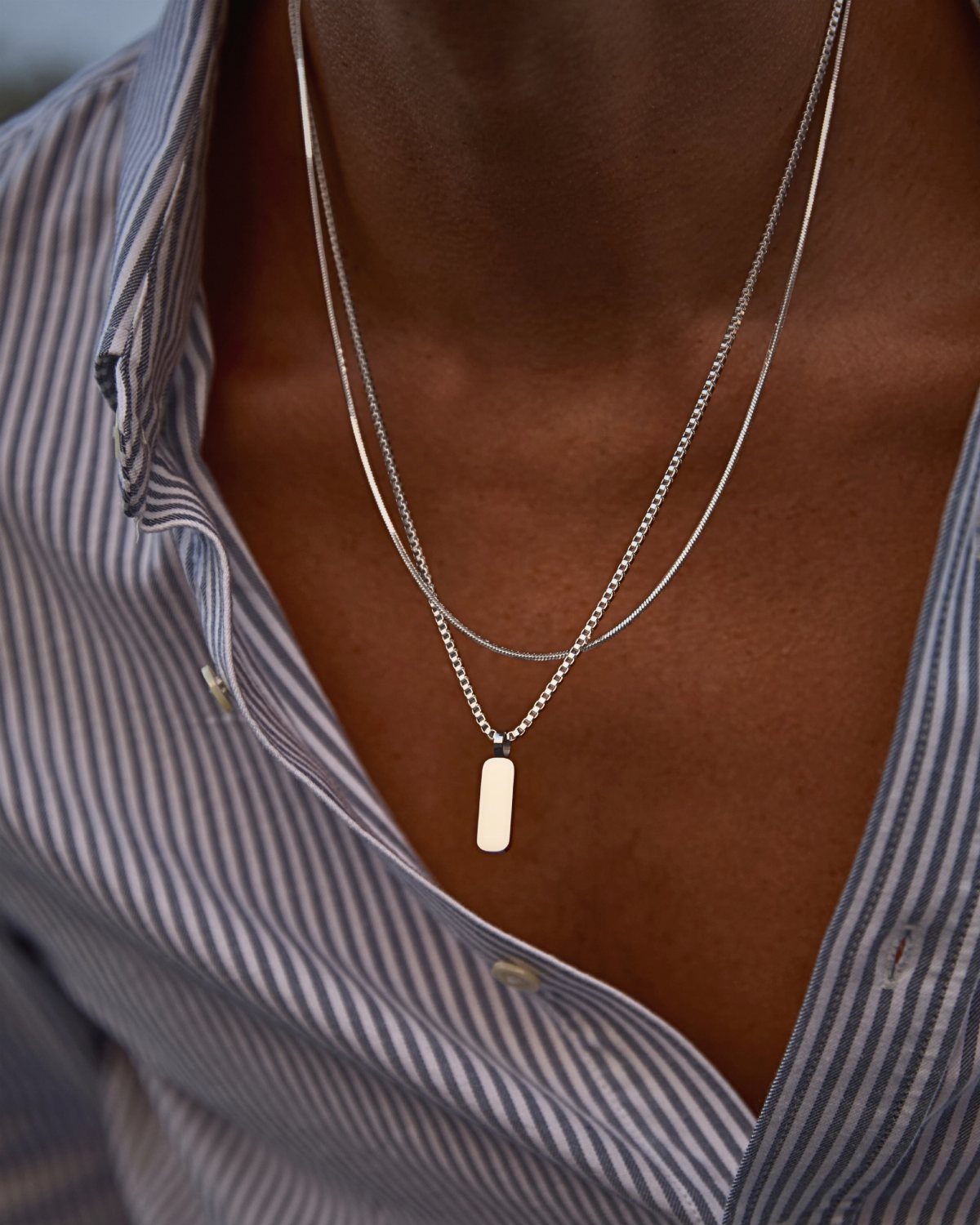 Two thin silver necklaces with a rectangular pendant on a man's chest